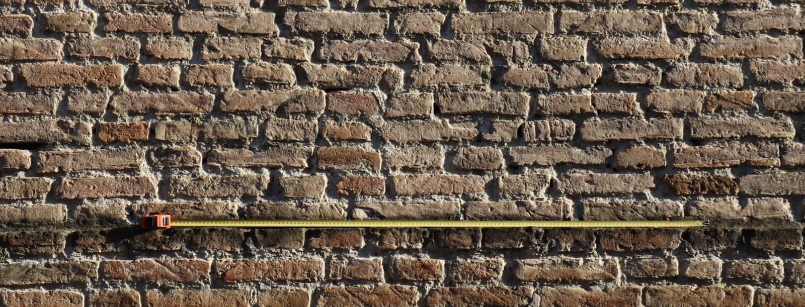 Muratura storica in mattoni a vista con un metro da cantiere appoggiato a un corso, durante il rilievo di un edificio in centro storico